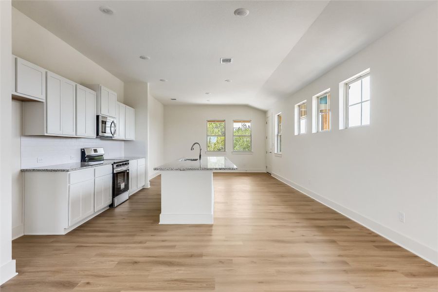 Kitchen featuring stainless steel appliances, an island with sink, white cabinets, light wood-type flooring, and light stone counters