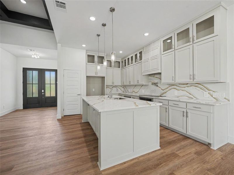 Contemporary kitchen featuring an island with a sink, white cabinetry, integrated appliances, and a marble-patterned backsplash