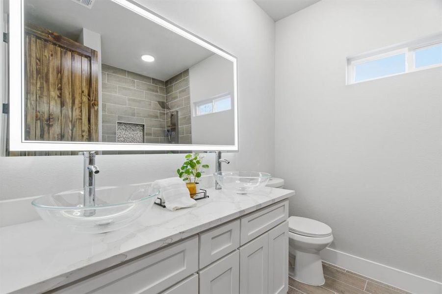 Bathroom with double vanity, wood finish floors, and a tile shower