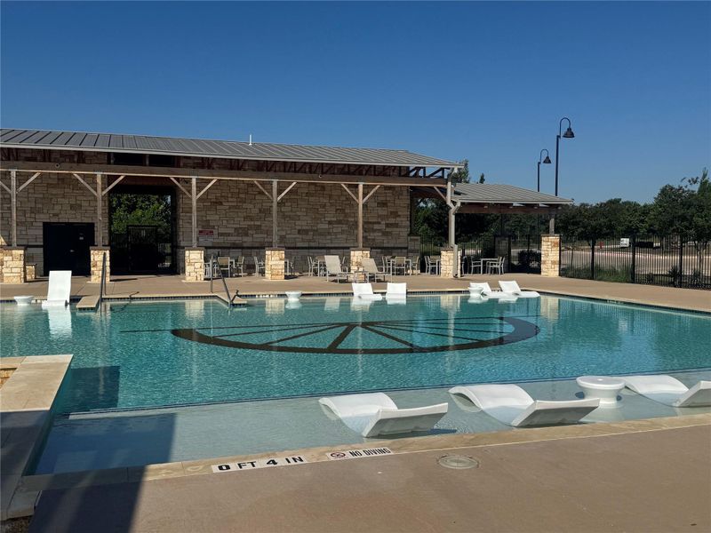 Resort-style swimming pool featuring in-pool lounge chairs, surrounding stone coping, and a deck with pergolas