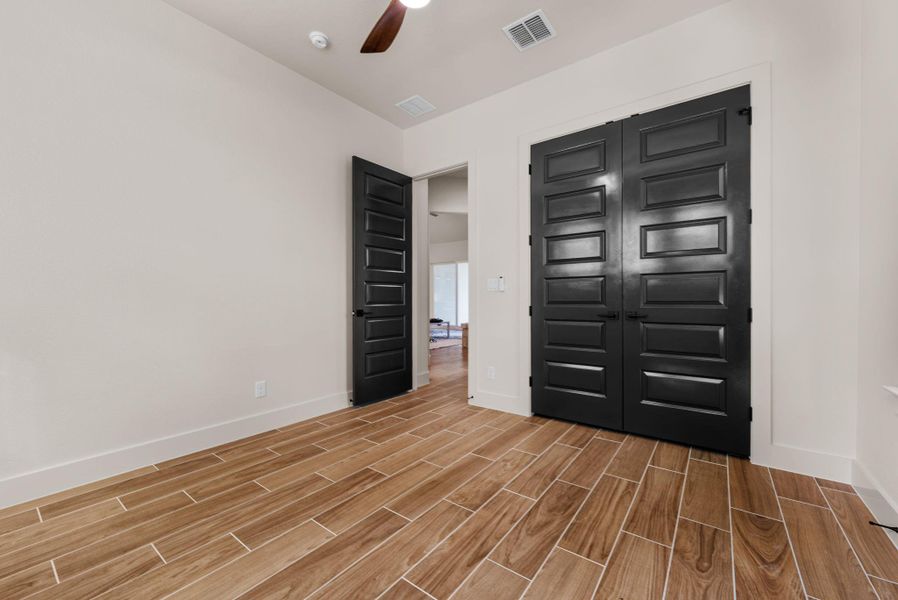 Rich wood-look flooring and dark paneled doors create a refined aesthetic in this versatile room.