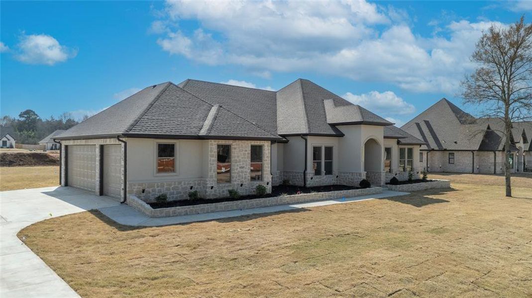 Back of property featuring stone siding, a yard, driveway, and stucco siding Back of property featuring stone siding, a yard, driveway, and stucco siding