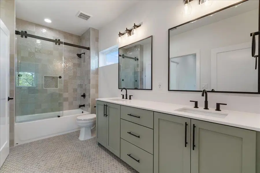Bathroom with enclosed tub / shower combo, double vanity, and light tile patterned floors