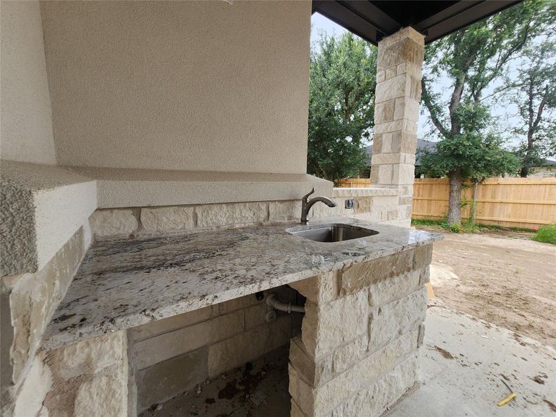 Outdoor kitchen counter featuring a built-in stainless steel sink, bronze-finish faucet, and a stone-clad base