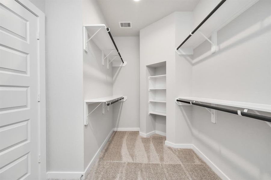 expansive walk-in closet, adorned with high ceilings and luxurious carpet. Immerse yourself in the inviting atmosphere created by warm paint tones, utilize the convenience of built-in shelving, and experience the modern and functional retreat accentuated by dark finishes. Sample photo of completed home with similar floor plan. As-built interior colors and selections may vary.