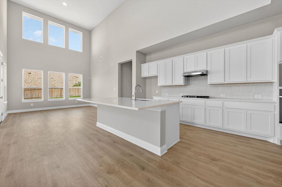 Kitchen with white cabinets, a high ceiling, a kitchen island with sink, tasteful backsplash, and light wood-type flooring