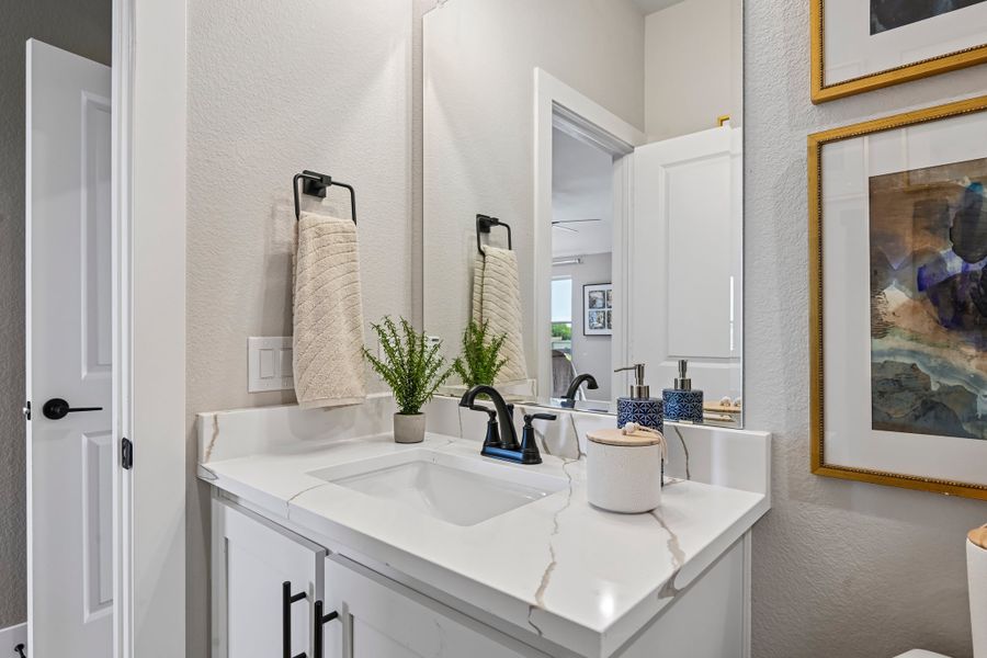 Bathroom vanity with white quartz countertop, black faucet, and large mirror above white cabinets