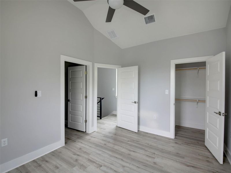 Unfurnished bedroom with a walk in closet, light wood finished floors, a ceiling fan, and high vaulted ceiling