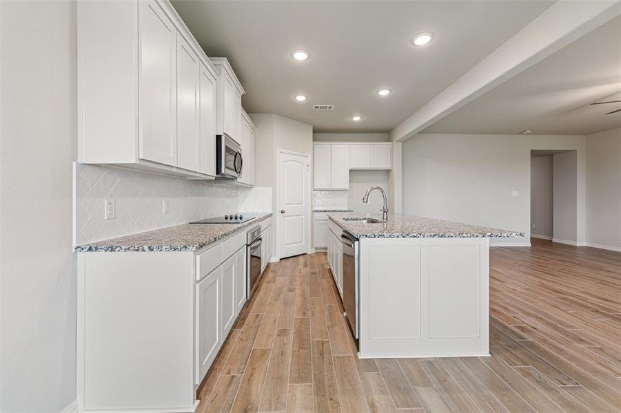 Kitchen with light stone countertops, backsplash, white cabinetry, recessed lighting, and light wood-style floors Kitchen with light stone countertops, backsplash, white cabinetry, recessed lighting, and light wood-style floors