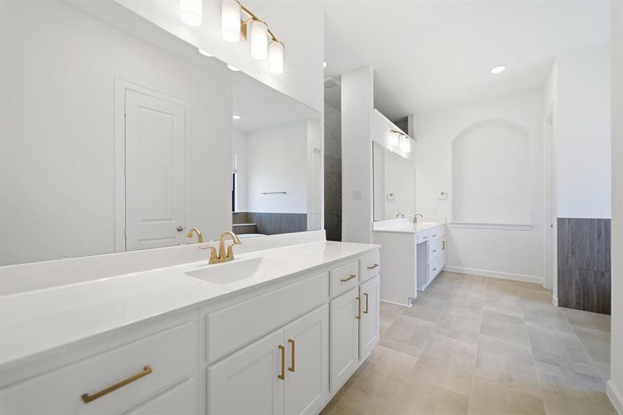 Spacious bathroom featuring dual vanities with white cabinetry and gold-toned hardware, white countertops, and a full-width mirror Spacious bathroom featuring dual vanities with white cabinetry and gold-toned hardware, white countertops, and a full-width mirror