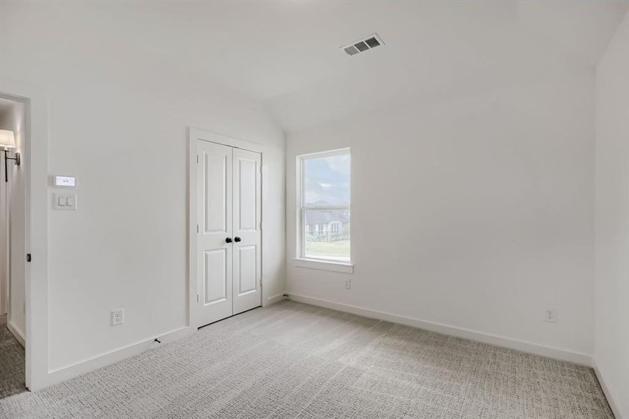 Unfurnished bedroom featuring light colored carpet, vaulted ceiling, and a closet