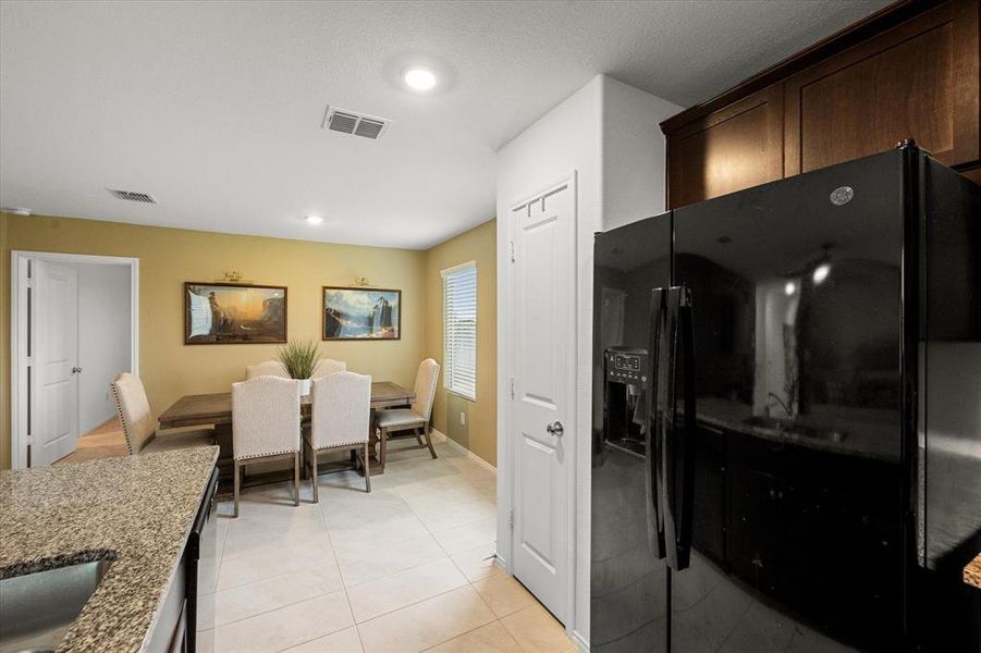 Kitchen featuring black refrigerator with ice dispenser, dark stone countertops, light tile patterned floors, and recessed lighting