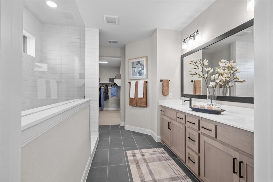 Full bathroom with double vanity, dark tile patterned flooring, walk in shower, and a spacious closet