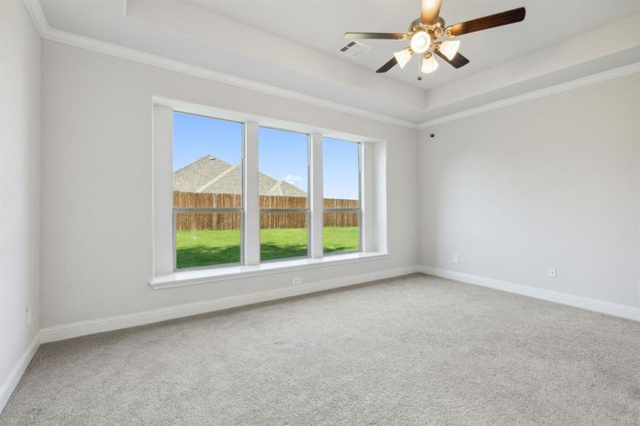 The Master bedroom has unique large windows, a raised ceiling, ceiling fan, and luxurious thick carpet.