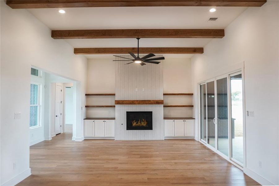 Unfurnished living room featuring beamed ceiling, a large fireplace, ceiling fan, and light hardwood / wood-style flooring