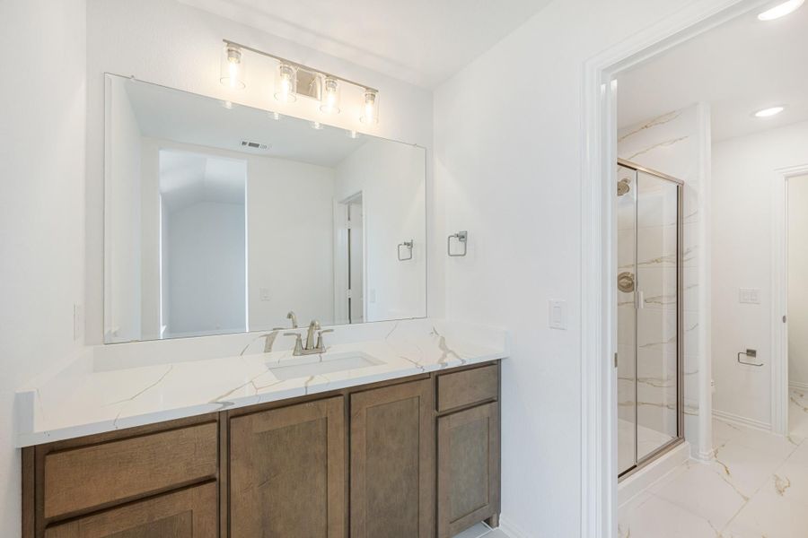 Bathroom with dark wood vanity, marble countertop, large mirror, and glass-enclosed shower in background. Bathroom with dark wood vanity, marble countertop, large mirror, and glass-enclosed shower in background.