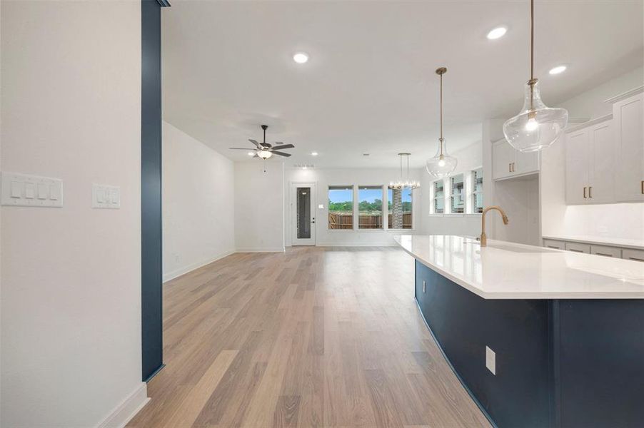 Open concept living area with light wood-style flooring, a ceiling fan, and large windows providing natural light