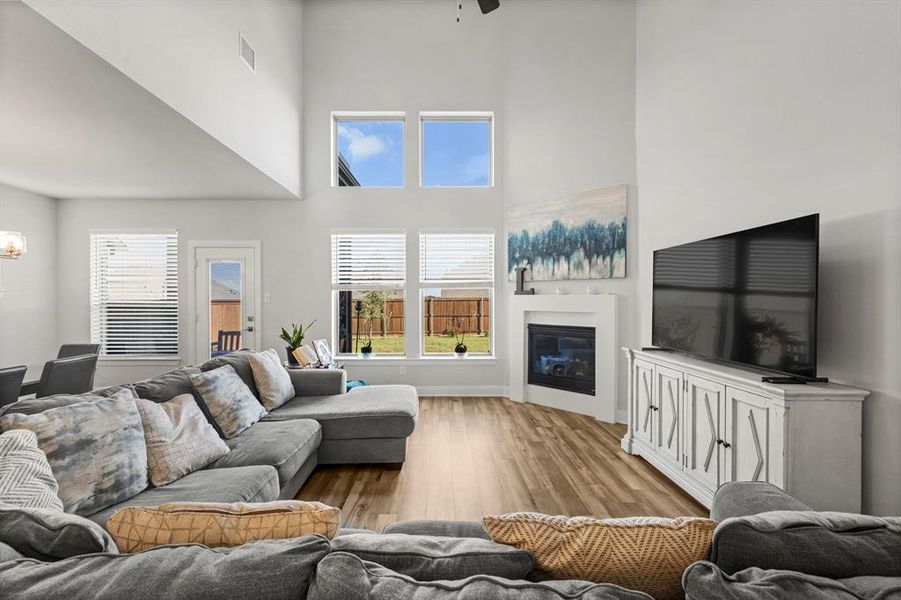 Living area featuring a towering ceiling, wood finished floors, plenty of natural light, a glass covered fireplace, and ceiling fan Living area featuring a towering ceiling, wood finished floors, plenty of natural light, a glass covered fireplace, and ceiling fan