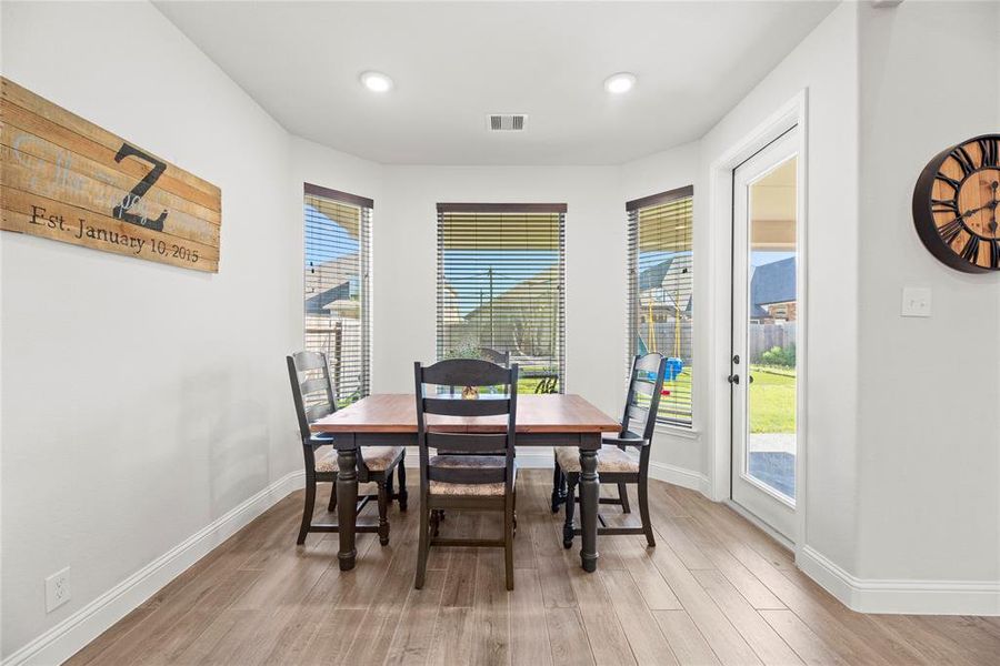 This is a bright and inviting dining space with large windows providing ample natural light, modern blinds for privacy, and a glass door leading to the backyard.