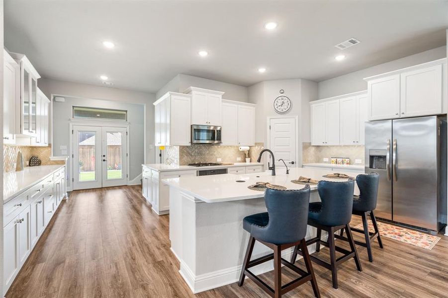 Modern kitchen featuring white cabinetry, stainless steel appliances, a center island with countertop seating, and wood-finish flooring Modern kitchen featuring white cabinetry, stainless steel appliances, a center island with countertop seating, and wood-finish flooring
