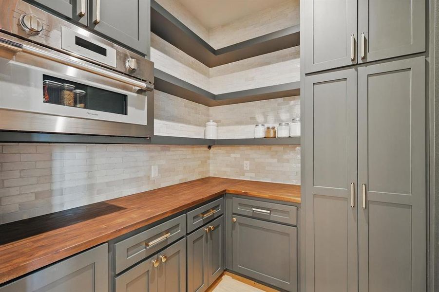 Kitchen featuring wooden counters, open shelves, stainless steel oven, tasteful backsplash, and gray cabinets Kitchen featuring wooden counters, open shelves, stainless steel oven, tasteful backsplash, and gray cabinets
