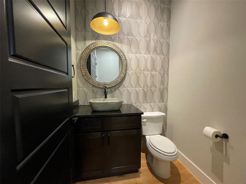 Powder room featuring a custom wall tile accent, black cabinet vanity with a dark stone countertop, and a vessel sink with a wall-mounted faucet