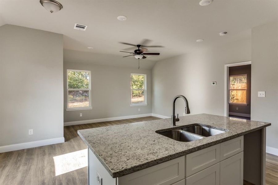 Kitchen with light stone counters, dark wood-style flooring, white cabinetry, an island with sink, and ceiling fan