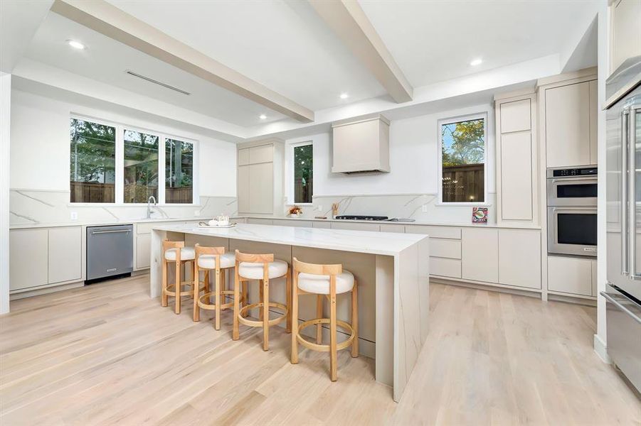 Kitchen with light stone counters, beam ceiling, modern cabinets, a kitchen breakfast bar, and light wood-style flooring Kitchen with light stone counters, beam ceiling, modern cabinets, a kitchen breakfast bar, and light wood-style flooring
