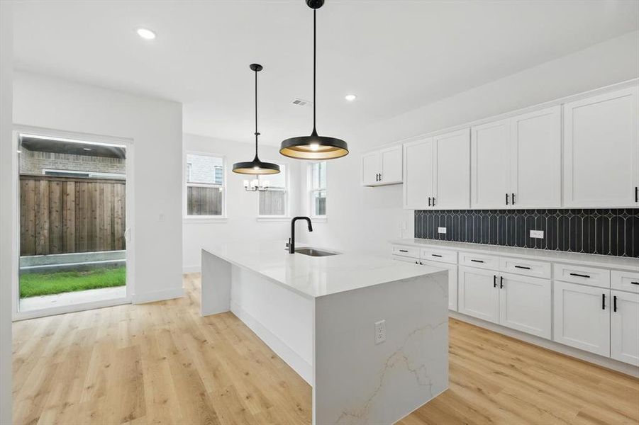 Kitchen featuring a sink, light wood-style flooring, decorative backsplash, white cabinetry, and light stone counters