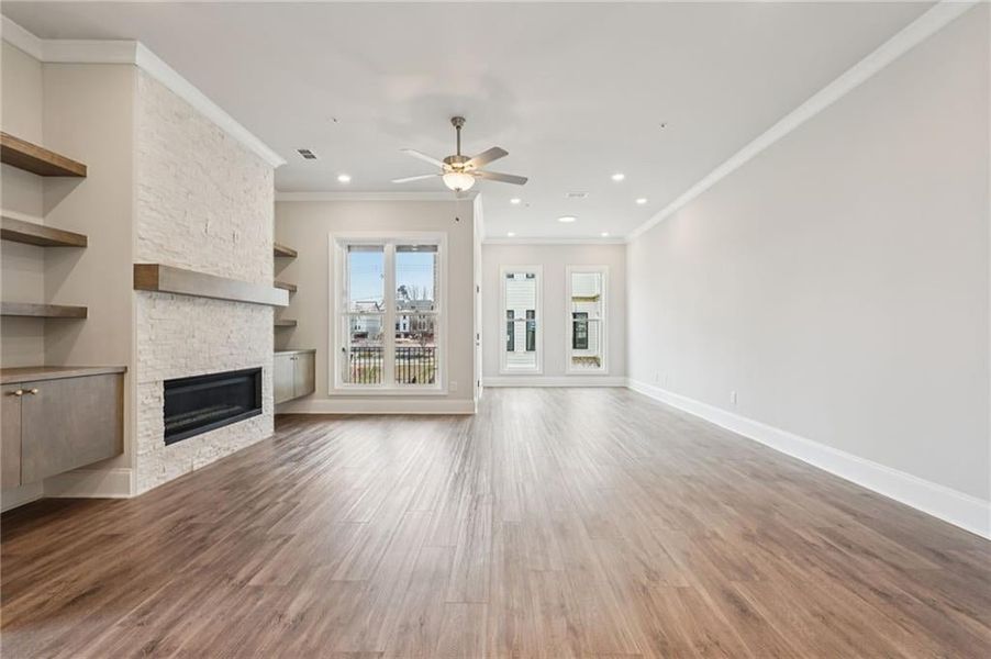 Unfurnished living room with a stone fireplace, crown molding, a ceiling fan, wood finished floors, and recessed lighting