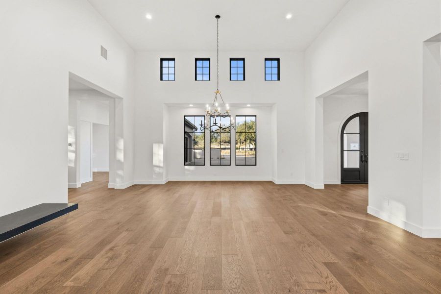 Unfurnished living room featuring a chandelier, light wood-style flooring, arched walkways, and a high ceiling