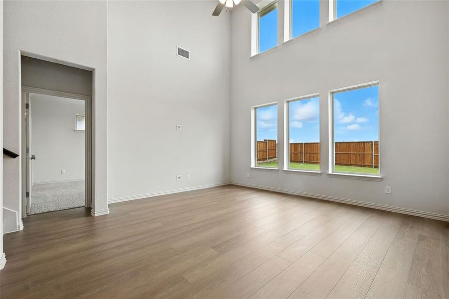 Unfurnished living room with wood finished floors, a ceiling fan, and a high ceiling