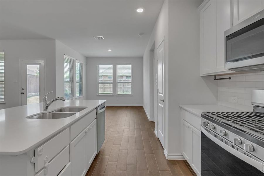 Kitchen featuring a center island with sink, appliances with stainless steel finishes, white cabinets, sink, and tasteful backsplash