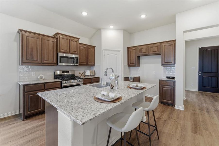 Kitchen featuring a large central island with seating, stainless steel appliances, dark wood cabinetry, white subway tile backsplash, and light wood-finish flooring