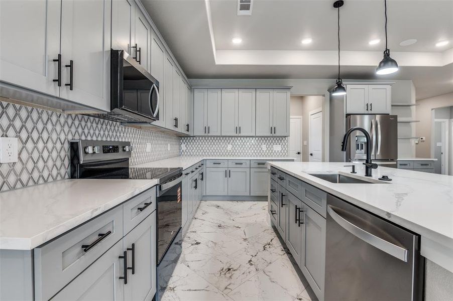 Kitchen featuring stainless steel appliances, decorative light fixtures, a raised ceiling, recessed lighting, and light stone countertops