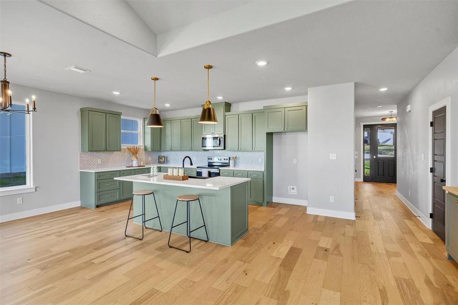 Kitchen featuring green cabinets, a chandelier, a breakfast bar, a kitchen island with sink, and recessed lighting Kitchen featuring green cabinets, a chandelier, a breakfast bar, a kitchen island with sink, and recessed lighting