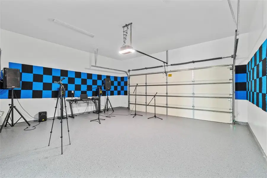 Garage space featuring acoustic paneling in a checkerboard pattern, a concrete floor with speckled finish, and an overhead garage door
