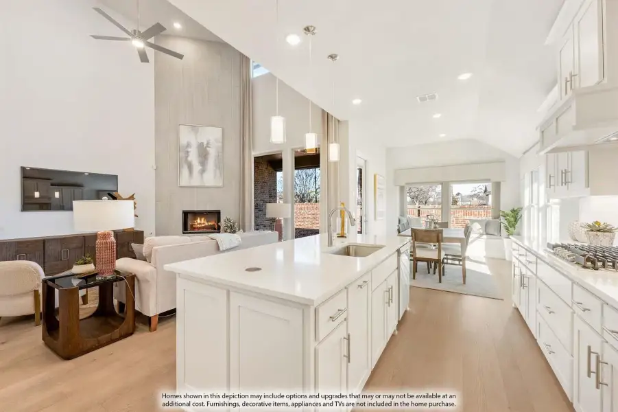 Open-concept kitchen with white island and cabinets, flowing into living room with tall fireplace and hardwood floors
