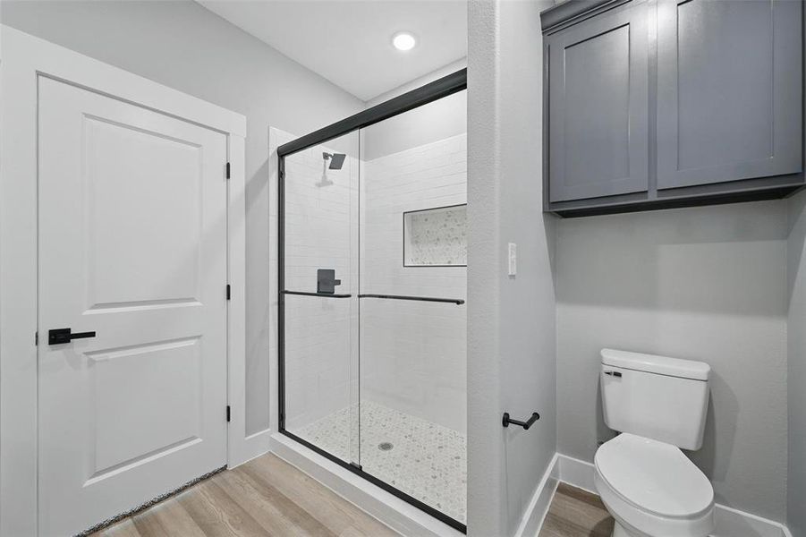 Bathroom with a shower stall, wood finished floors, toilet, and baseboards