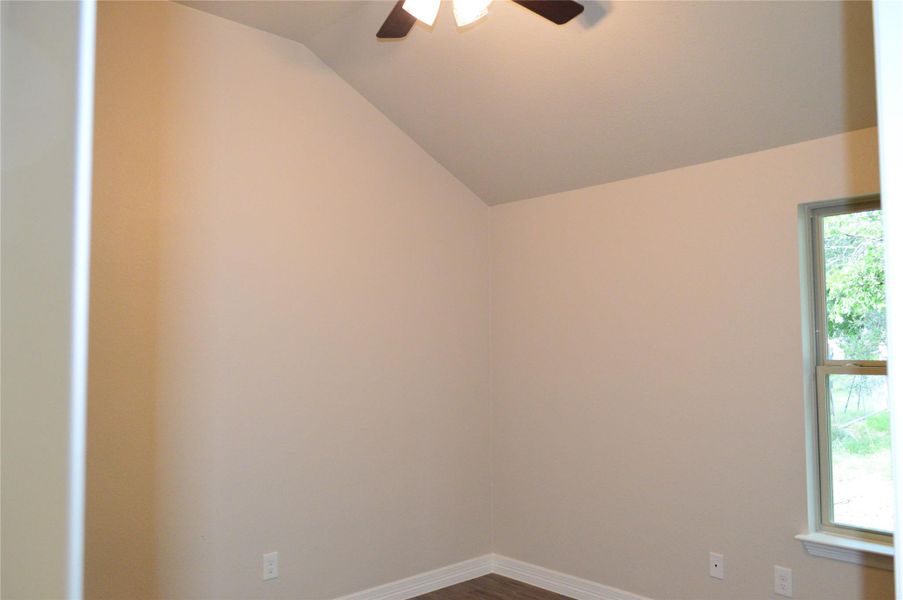 Unfurnished room featuring ceiling fan, lofted ceiling, and dark wood-type flooring