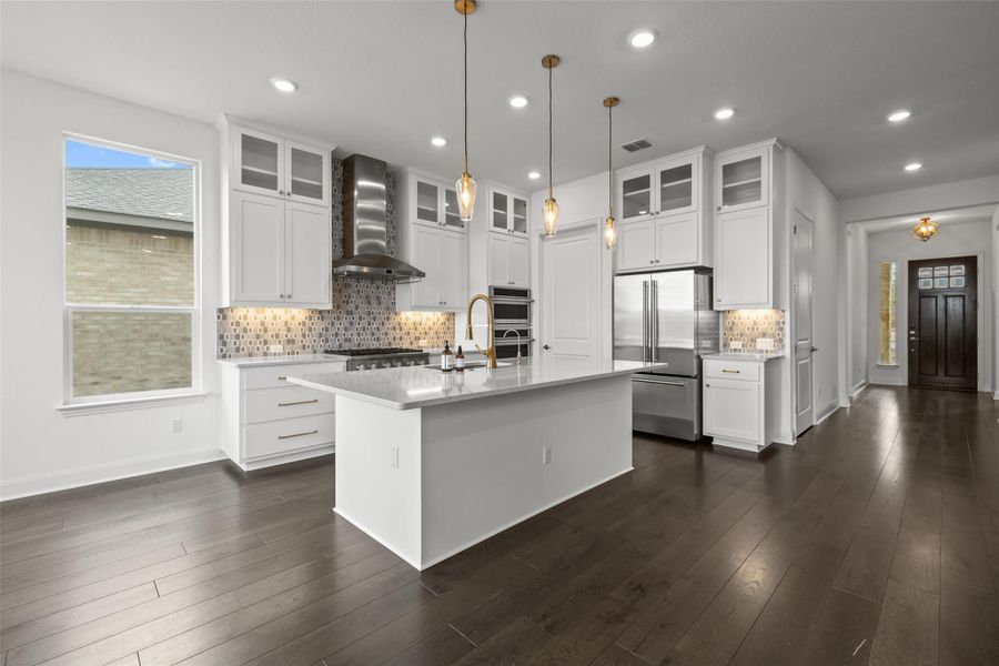 Kitchen with wall chimney range hood, a kitchen island with sink, light countertops, and appliances with stainless steel finishes