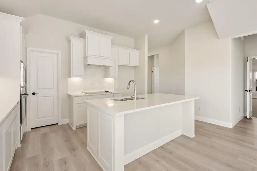 Kitchen with white cabinets, large island with sink, and light wood floors