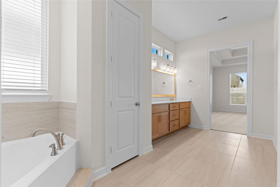 This view of the primary bathroom highlights the extended vanity area and soaking tub, thoughtfully designed with space and comfort in mind, creating a spa inspired setting that feels bright, open, and relaxing.