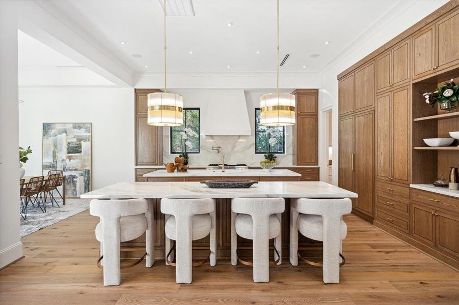 This chef's kitchen is a masterpiece, featuring SubZero and Wolf appliances, stunning stained white oak cabinetry, and Ralph Lauren brass pendants for a touch of elegance. Dual islands with Dekton quartz countertops offer ample space for meal prep and breakfast bar seating, combining style with practicality.