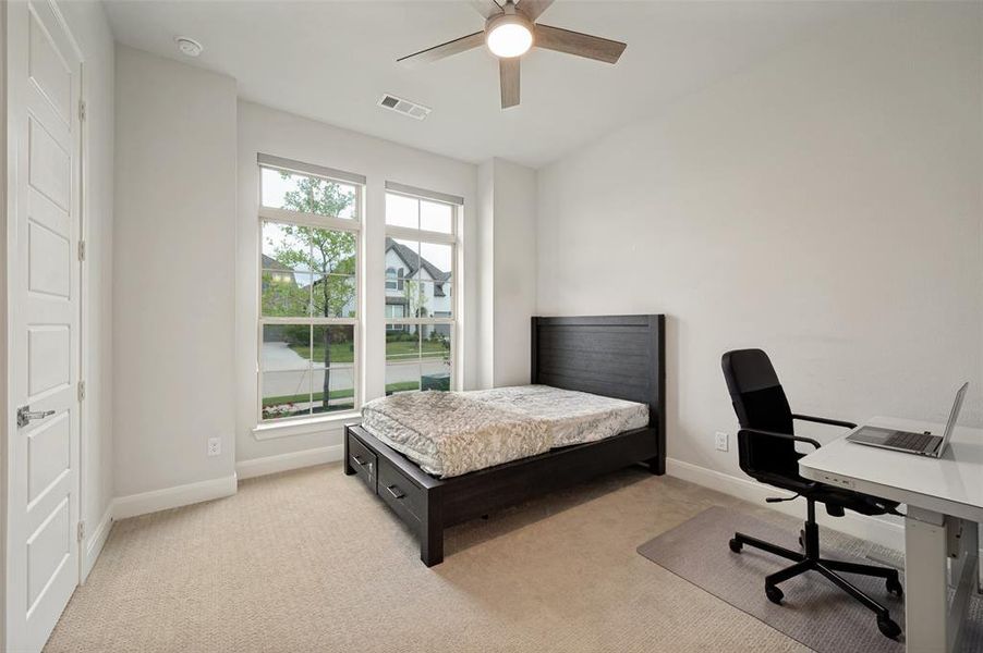 Bright room featuring two large windows, neutral carpeting, a ceiling fan with integrated lighting, and a five-panel interior door