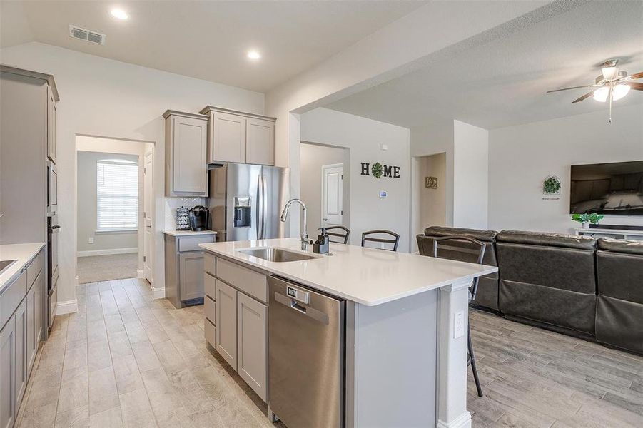 Kitchen with an island with sink, gray cabinets, and appliances with stainless steel finishes