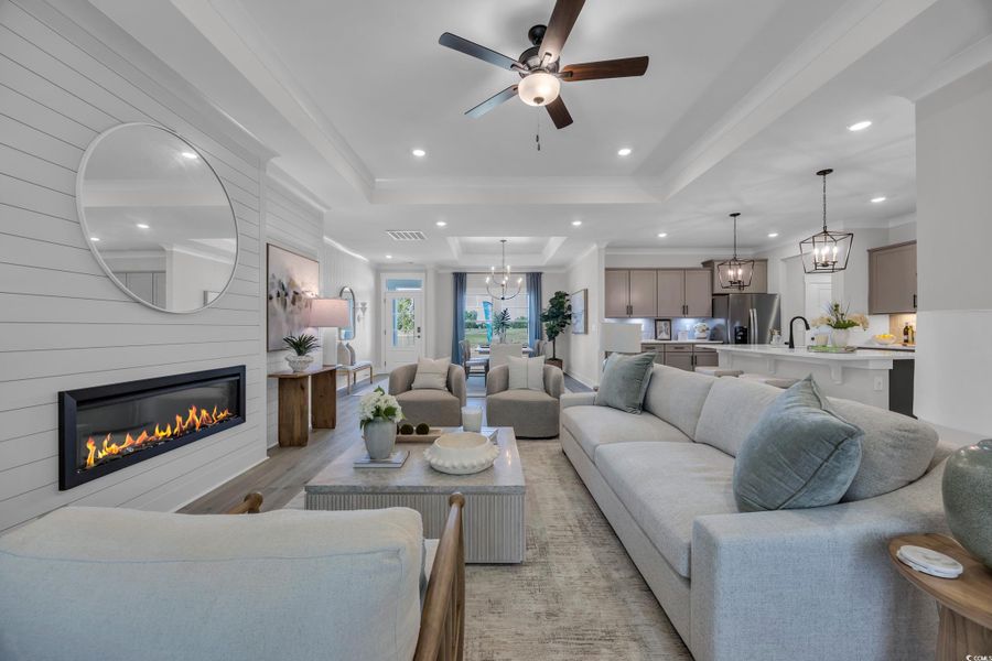 Living room featuring a chandelier, a tray ceiling, recessed lighting, crown molding, and a large fireplace