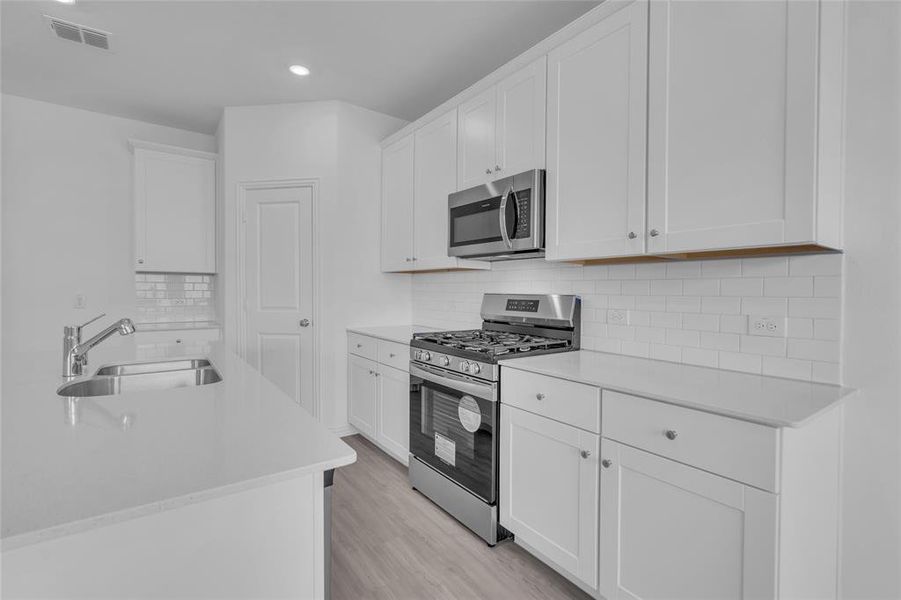 Kitchen featuring appliances with stainless steel finishes, light hardwood / wood-style floors, tasteful backsplash, white cabinets, and sink