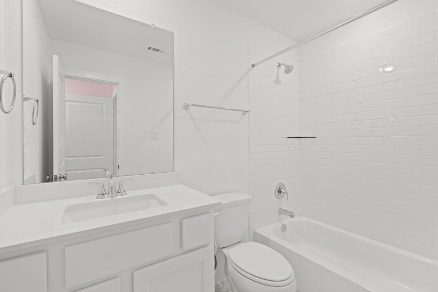 Located off the upstairs second bedroom, this full bathroom features white cabinets, a spacious tub and shower with subway tile, and large mirror.