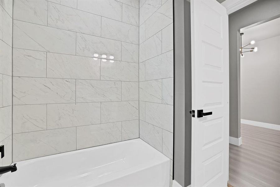 Bathroom with wood-type flooring, tiled shower / bath combo, and an inviting chandelier